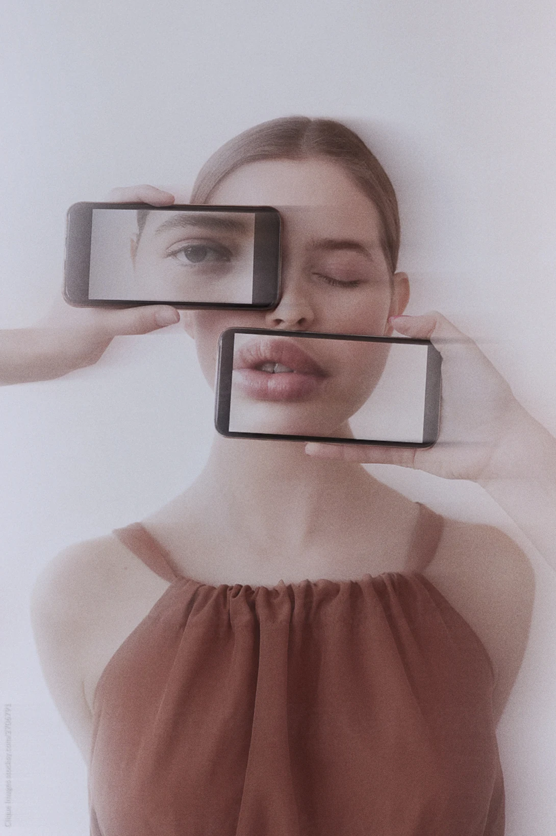 A face partially reflected and obscured by phones.